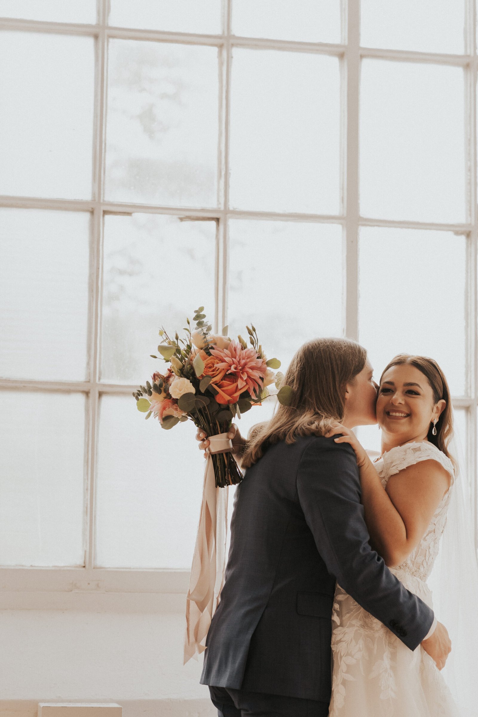 bride kissing bride holding orange fall wedding flowers